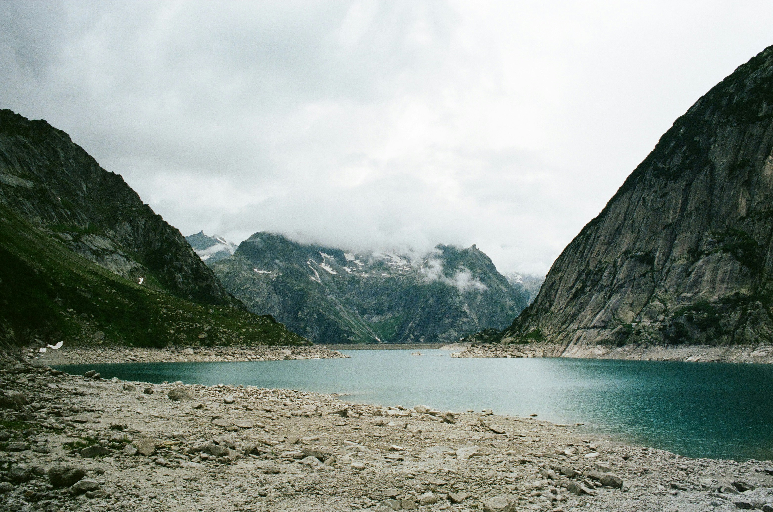 lake near mountain under white sky during daytime